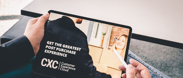 We look over a shoulder at a tablet on which the Customer Experience Cloud is advertised as "Get the greatest post purchase experience".